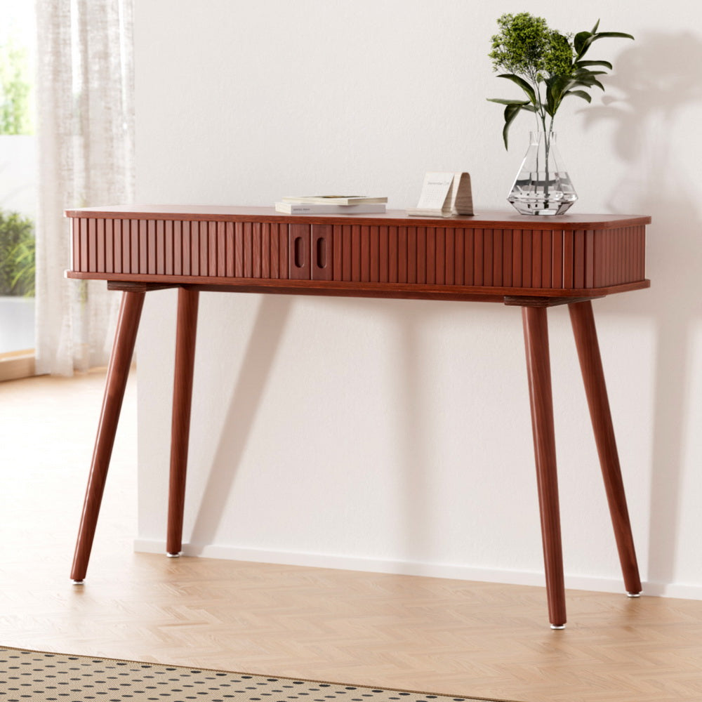 Console table in walnut finish with fluted drawer front and angled tapered legs, styled with books and glass vase in room