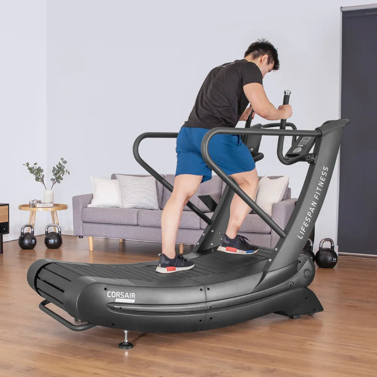 Man using FreeRun 105 treadmill with kettlebells and couch visible in home gym space