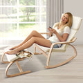 Woman reclining in cream bentwood rocking chair with footrest, holding phone, bright room with large window and curtains