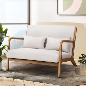 Cream fabric two-seater loveseat with solid wood curved armrests, two cushions, in living room with window and plants