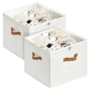 Two cream fabric shoe storage boxes with clear zipper lids and tan leather handles loaded with shoes on white background