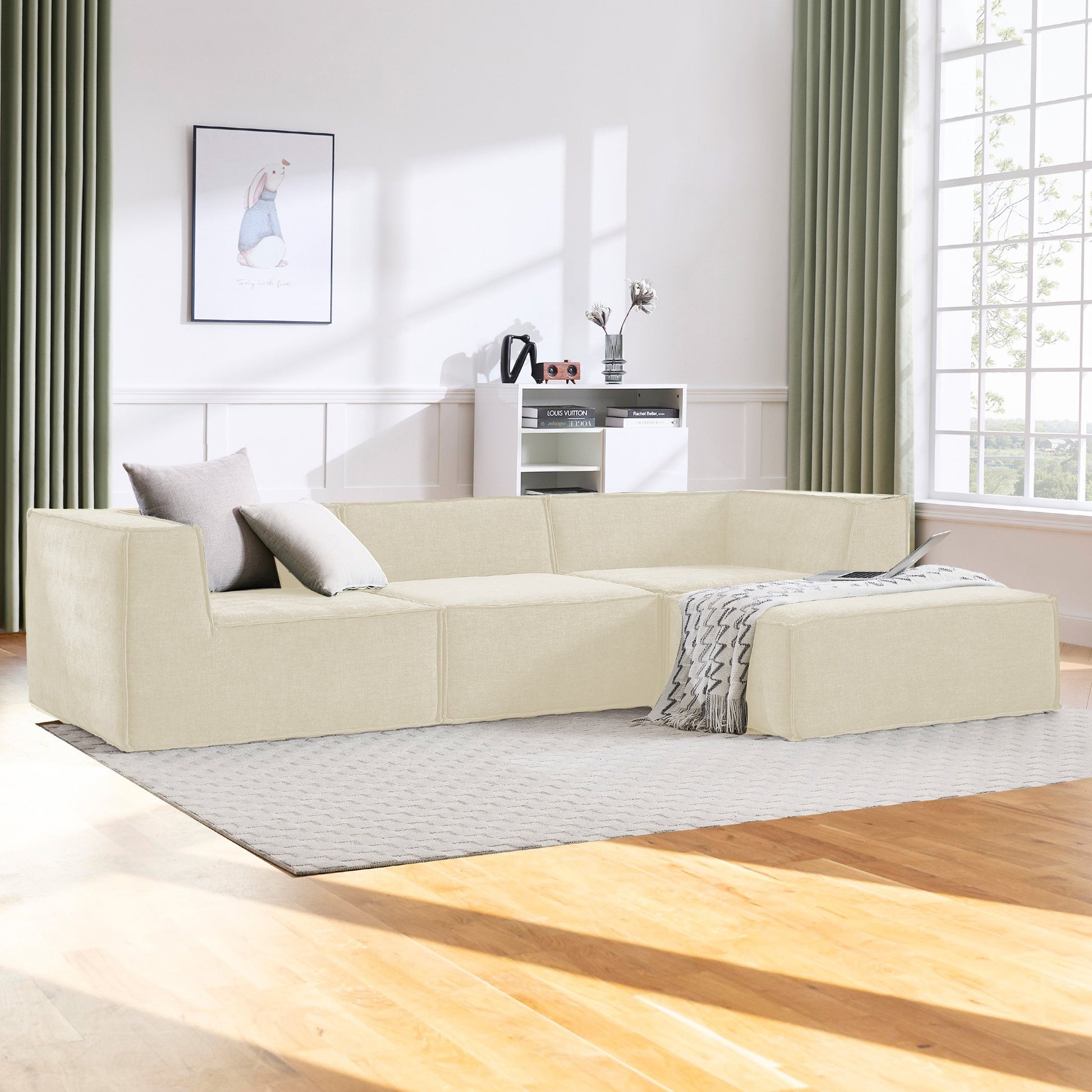 Cream modular sofa with grey cushions in sunlit living room, green curtains, timber floor, patterned throw on ottoman