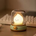 Smiley face raindrop LED lamp inside cylindrical glass dome on mint green base with gold knob on desk