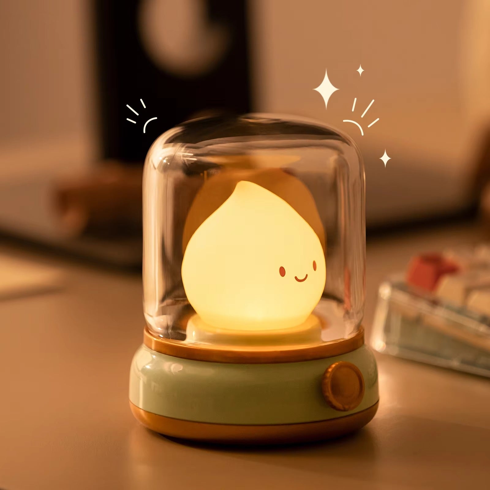 Raindrop LED lamp on mint green base with sparkle graphics glowing on warm-lit desk with blurred items in background