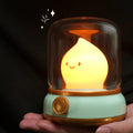 Raindrop LED lamp on mint green base glowing amber yellow being held in palm against black background