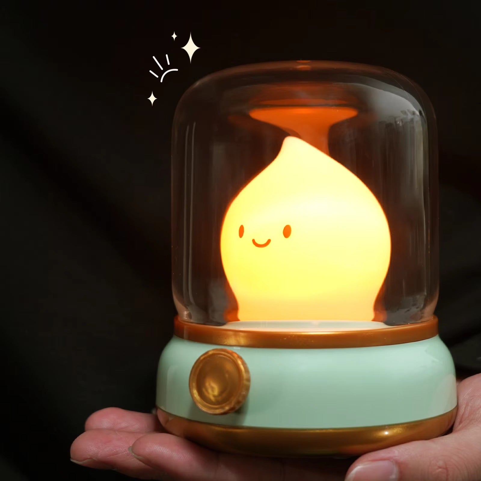 Raindrop LED lamp on mint green base glowing amber yellow being held in palm against black background