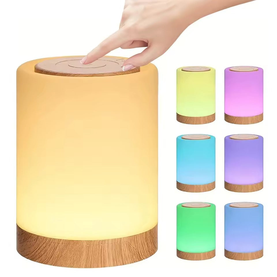 Cylindrical bedside lamp glowing warm on wooden nightstand beside bed, hand pointing at touch top, Mini Touch Lamp text