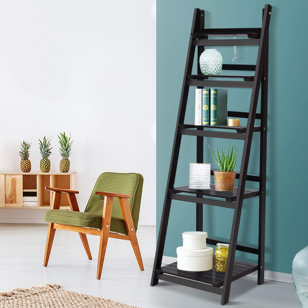 Dark espresso 5-tier A-frame ladder shelf styled with books, aloe plant and hat boxes against teal wall beside armchair