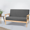 Dark grey fabric two-seater sofa beside wooden round side table with green plant, white wall lifestyle setting