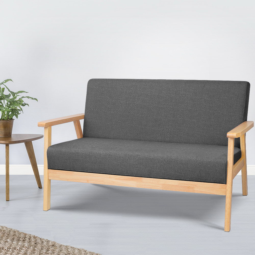 Dark grey fabric two-seater sofa beside wooden round side table with green plant, white wall lifestyle setting