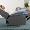Woman reclining fully in dark grey PU recliner with footrest extended and side pocket visible, teal carpet, living room