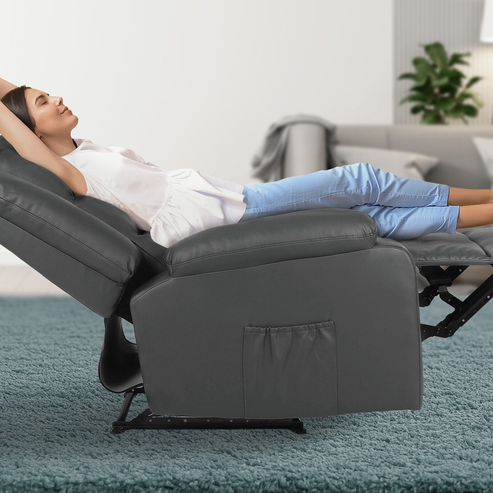 Woman reclining fully in dark grey PU recliner with footrest extended and side pocket visible, teal carpet, living room