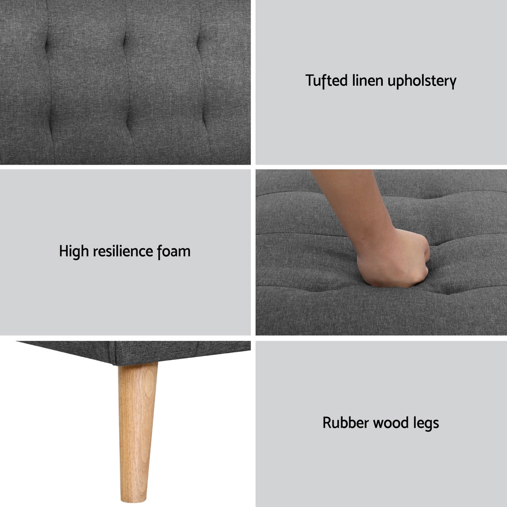 Dark grey tufted sofa bed in flat position in living room with wooden floors and area rug
