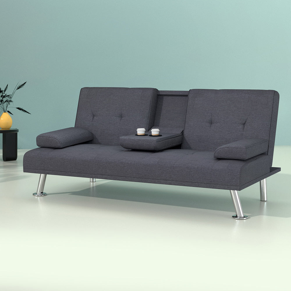 Dark grey fabric sofa bed with centre cup holder tray and two coffees against teal wall with yellow vase