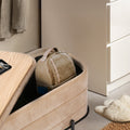 Beige velvet storage ottoman bench open with a bag and blue phone stored inside, wood tray with keys alongside in a bedroom