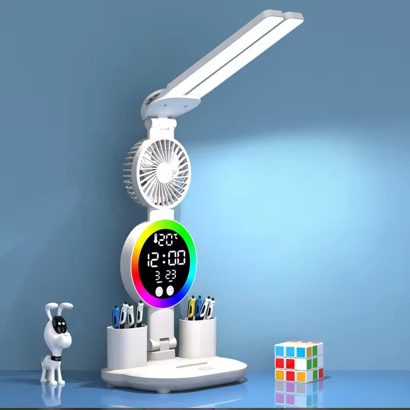 White desk lamp with LED bar, fan, RGB clock display, dual pen holders on desk with toy dog figure and Rubiks cube
