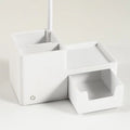 White desk lamp base with two open pen holder compartments, flat shelf and pull-out drawer, power button on front