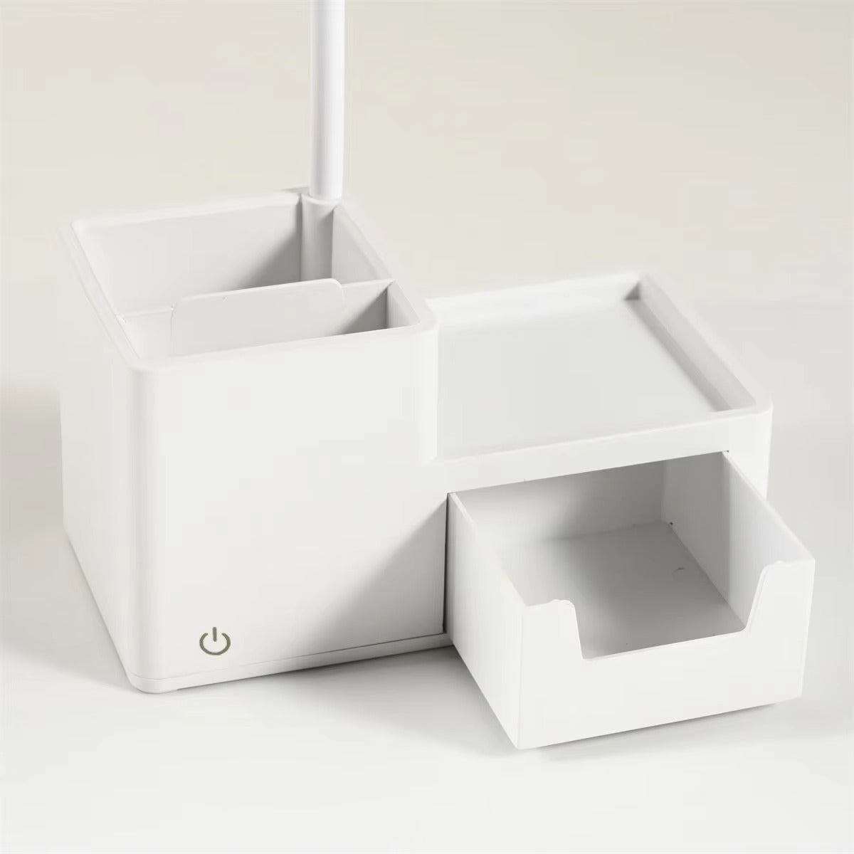 White desk lamp base with two open pen holder compartments, flat shelf and pull-out drawer, power button on front