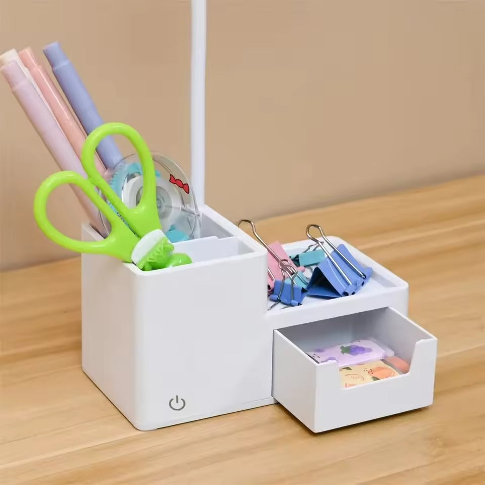 Desk lamp organizer base filled with pens, scissors and tape in pen holder, binder clips on shelf, stickers in open drawer
