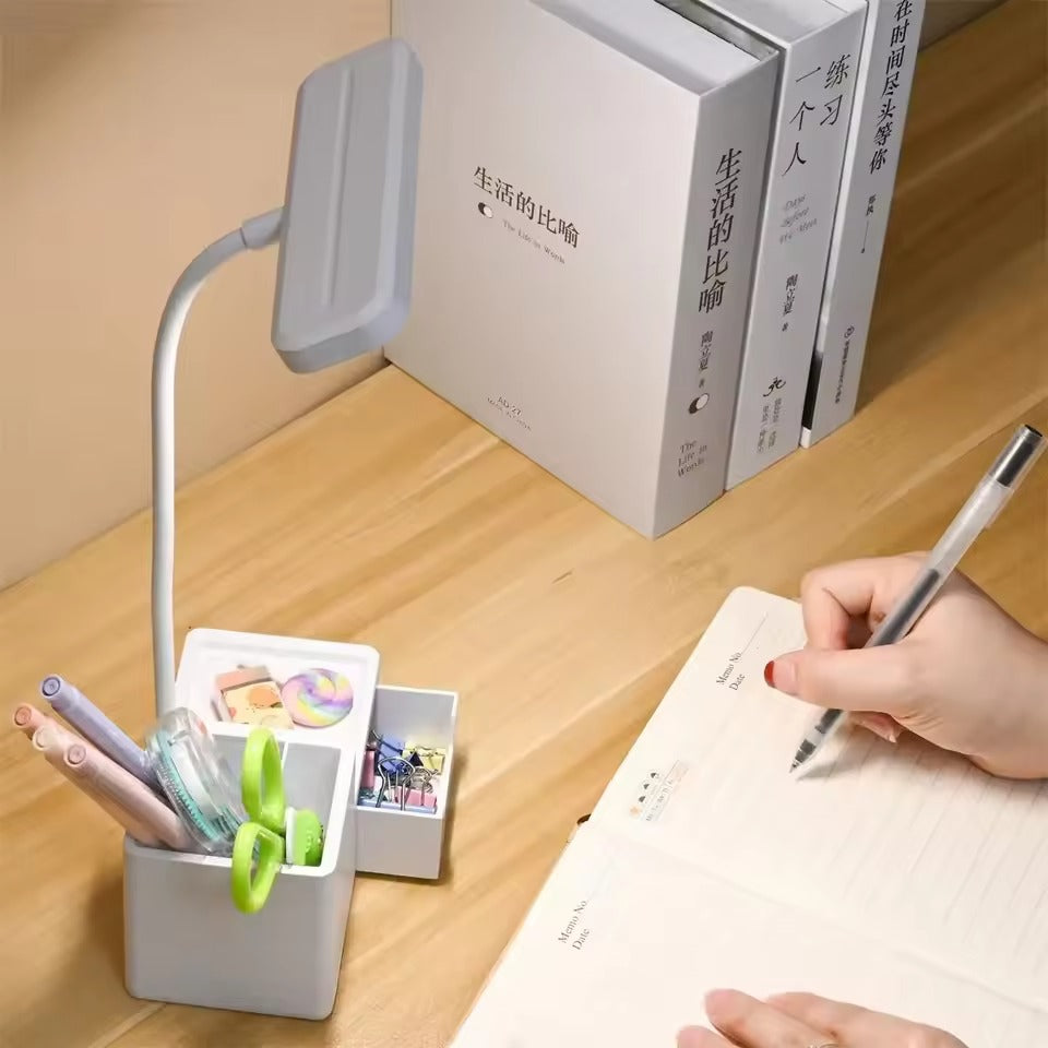 White flexible neck desk lamp with filled organizer base on wooden desk, hand writing in notepad with Chinese books behind