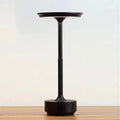 Matte black slim-stem table lamp with flat disc shade on wooden surface, knurled stem and USB-C port on circular base