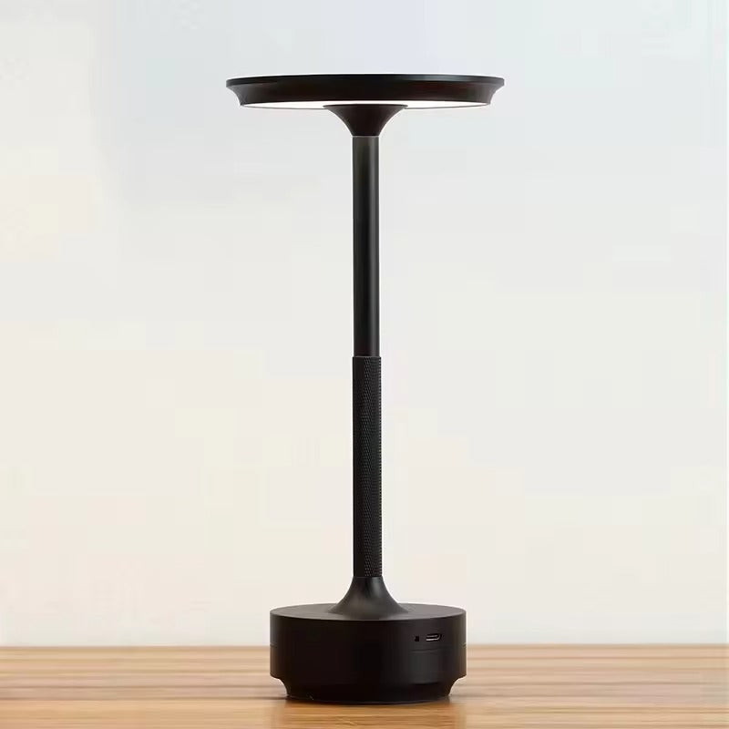 Matte black slim-stem table lamp with flat disc shade on wooden surface, knurled stem and USB-C port on circular base