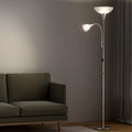 Silver dual-shade floor lamp with both shades lit beside dark green sofa in dim living room with curtains