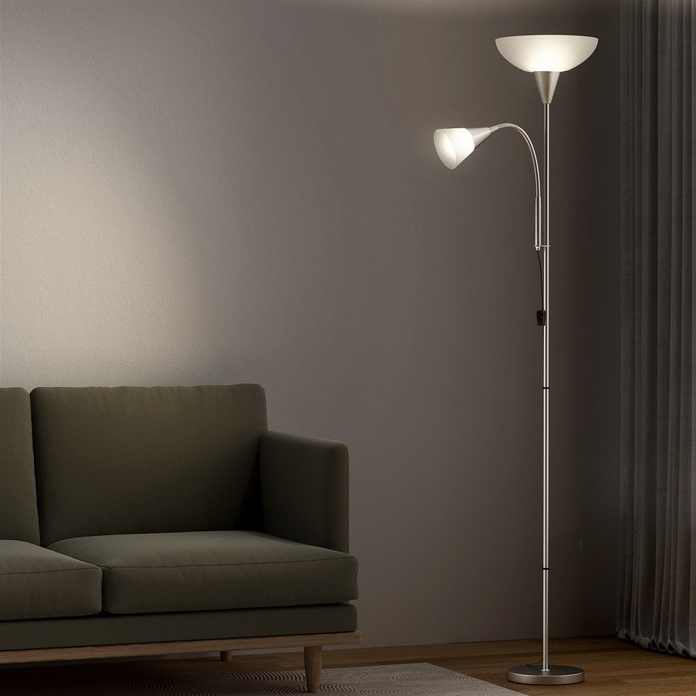 Silver dual-shade floor lamp with both shades lit beside dark green sofa in dim living room with curtains