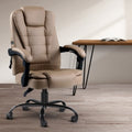 Beige PU executive massage chair in room lifestyle setting next to timber hairpin leg desk with open book, warm light