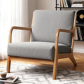 Grey fabric armchair with natural wood open-arm frame in reading room with record shelf and patterned rug