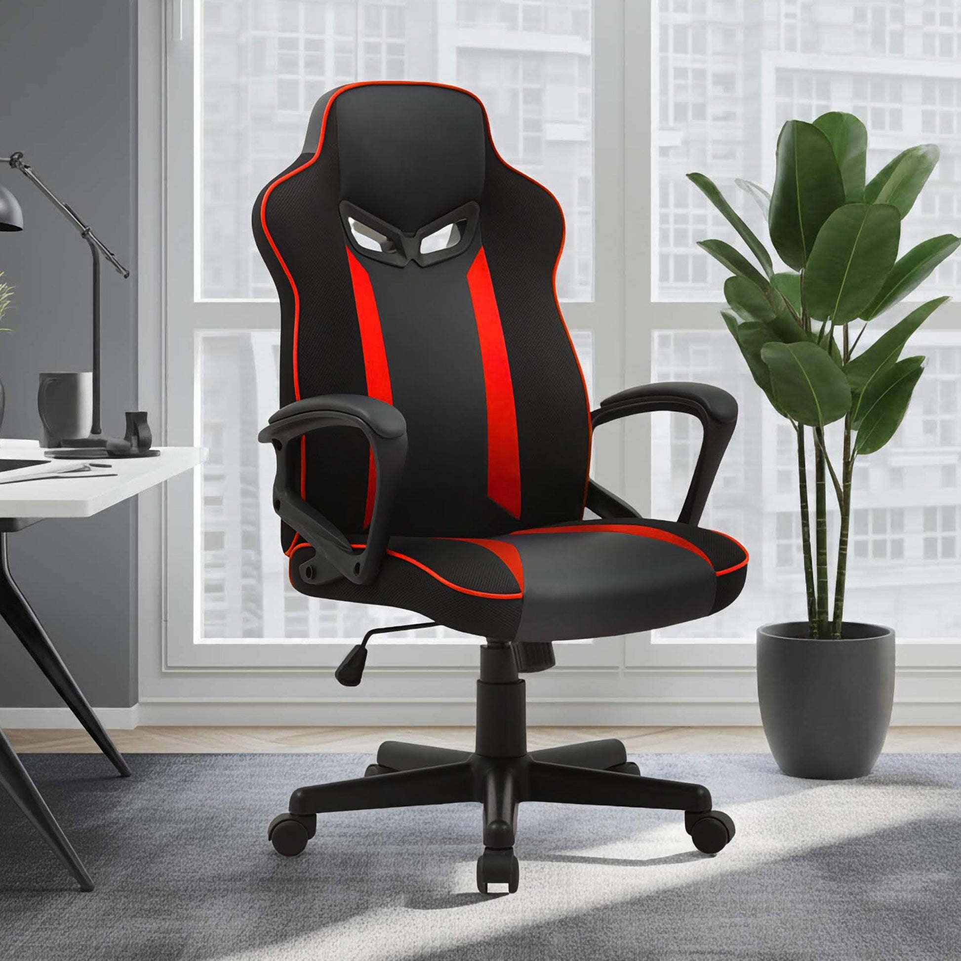 Black and red gaming office chair in modern room with large window, plant and herringbone floor, three-quarter view