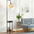 Arc shelf floor lamp with cream linen shade and two walnut tiers styled with books and decor next to grey sofa