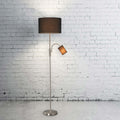 Dual-shade floor lamp with black drum and reading arm against white brick wall on concrete floor