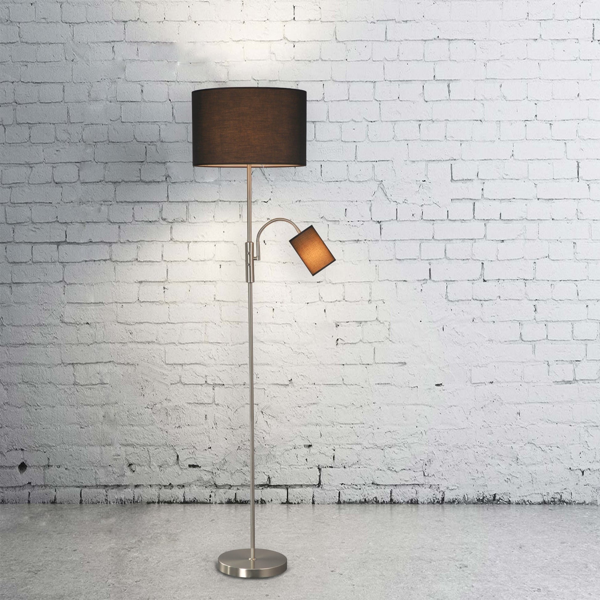 Dual-shade floor lamp with black drum and reading arm against white brick wall on concrete floor