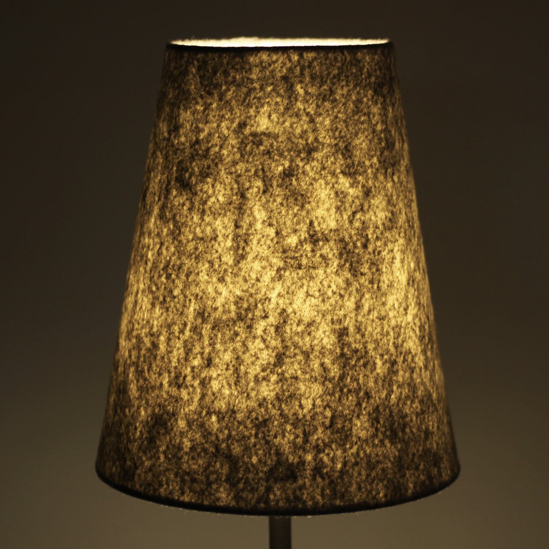 Close-up of conical grey felt lampshade glowing warm amber from internal light on dark background