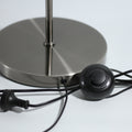 Close-up of brushed chrome round lamp base with black power cord, inline push switch and plug on light grey surface