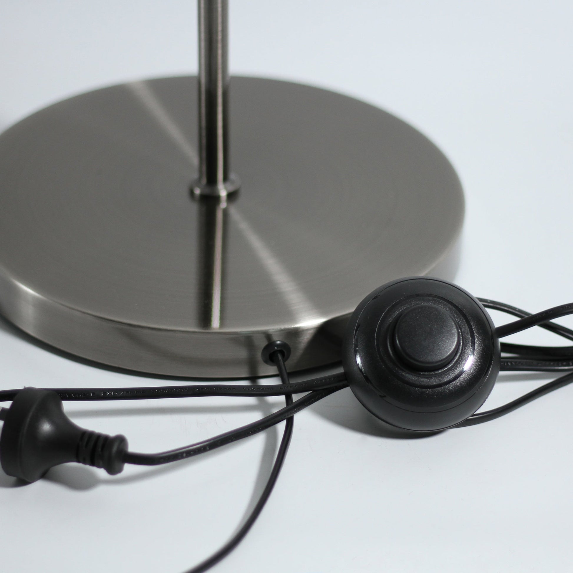Close-up of brushed chrome round lamp base with black power cord, inline push switch and plug on light grey surface
