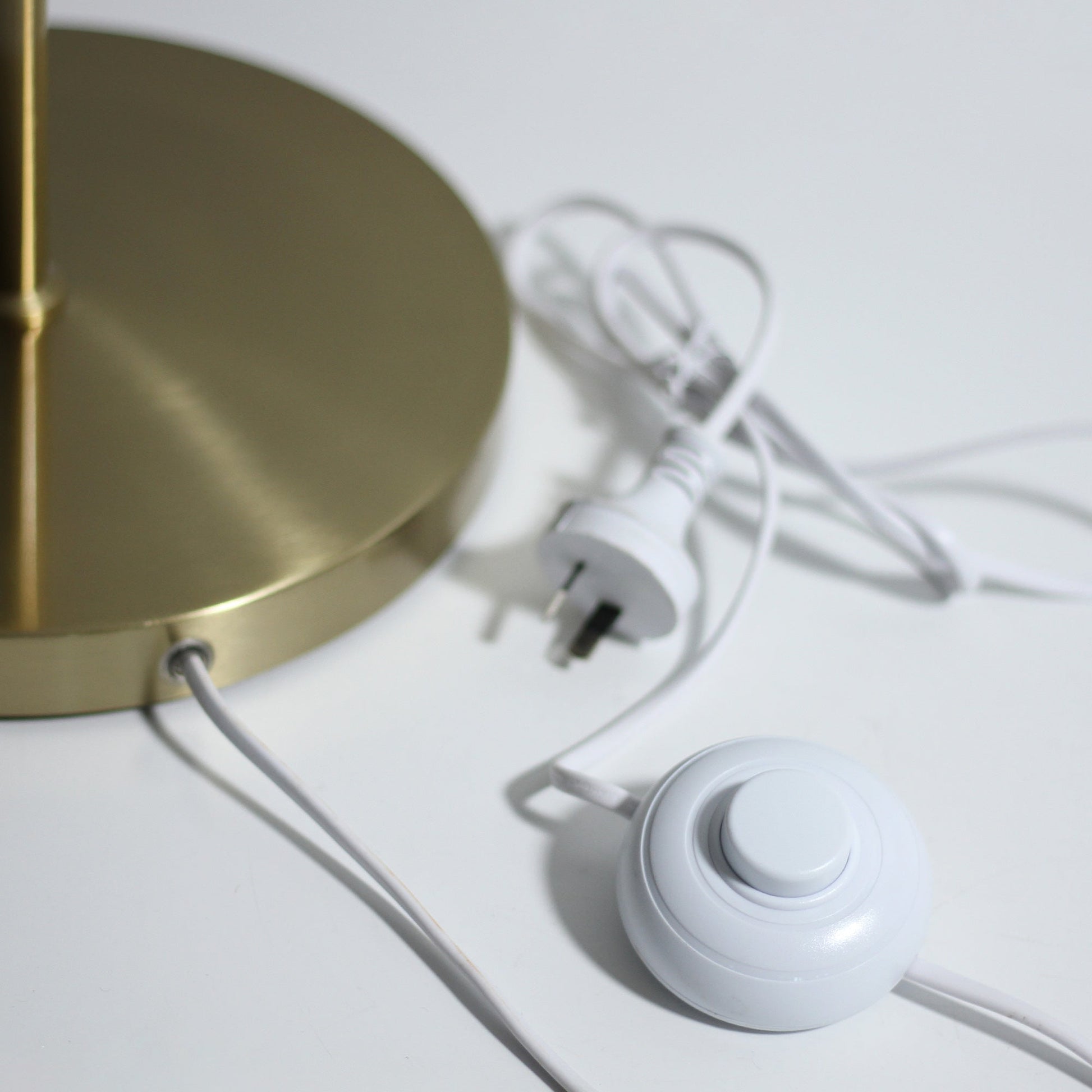 Close-up of brushed gold round lamp base with white power cord, inline foot switch and Australian plug on white surface
