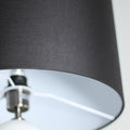 Close-up of dark grey drum shade, black exterior with white interior lining and chrome fitting above glass ball
