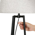 Hand pulling cord switch on black square-frame tripod floor lamp base with grey fabric shade