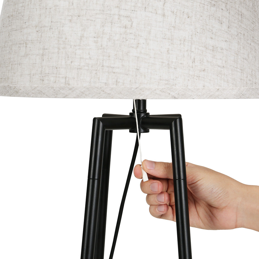 Hand pulling cord switch on black square-frame tripod floor lamp base with grey fabric shade