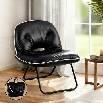 Black foldable floor chair with tufted back and white piping in room setting by window, inset shows folded bag form