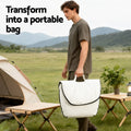 Man carrying folded white floor chair as a portable bag at campsite, text reads 