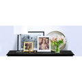 Black console table top surface styled with photo frames, lamp, decorative plate and pink flower vase