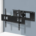 Full-motion TV wall bracket extended arms mounted on blue-grey corner wall with spirit level on TV plate