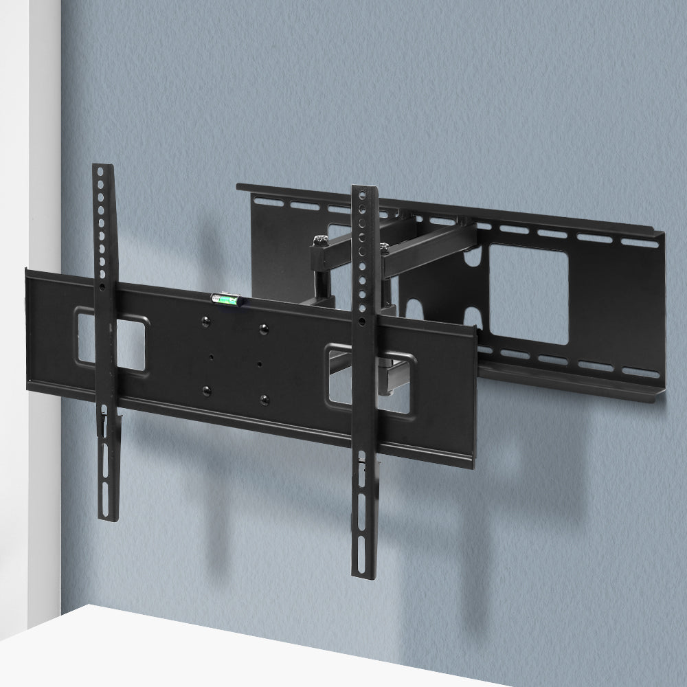 Full-motion TV wall bracket extended arms mounted on blue-grey corner wall with spirit level on TV plate