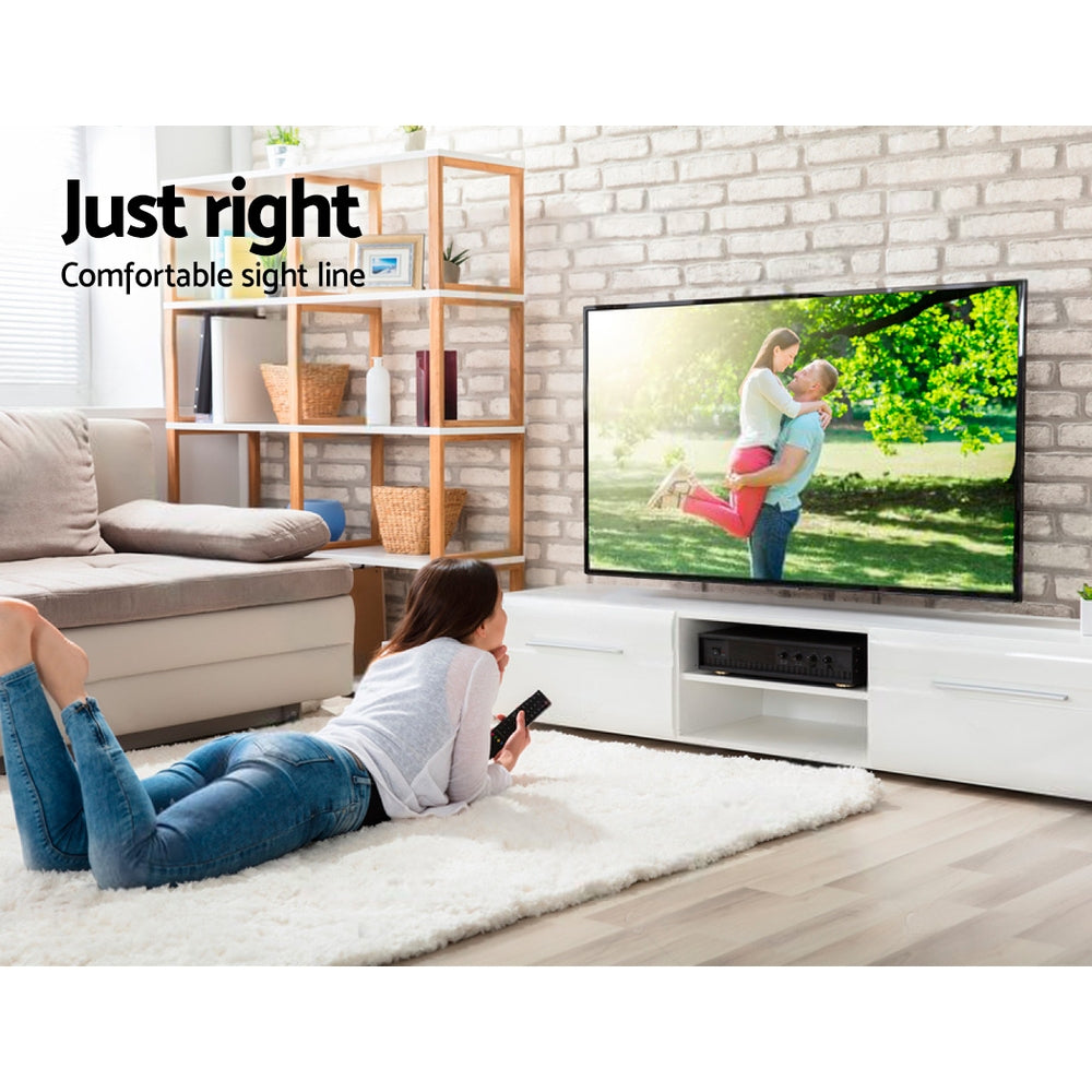 Full-motion TV bracket lifestyle woman lying on white rug watching TV on white brick wall with oak bookshelf
