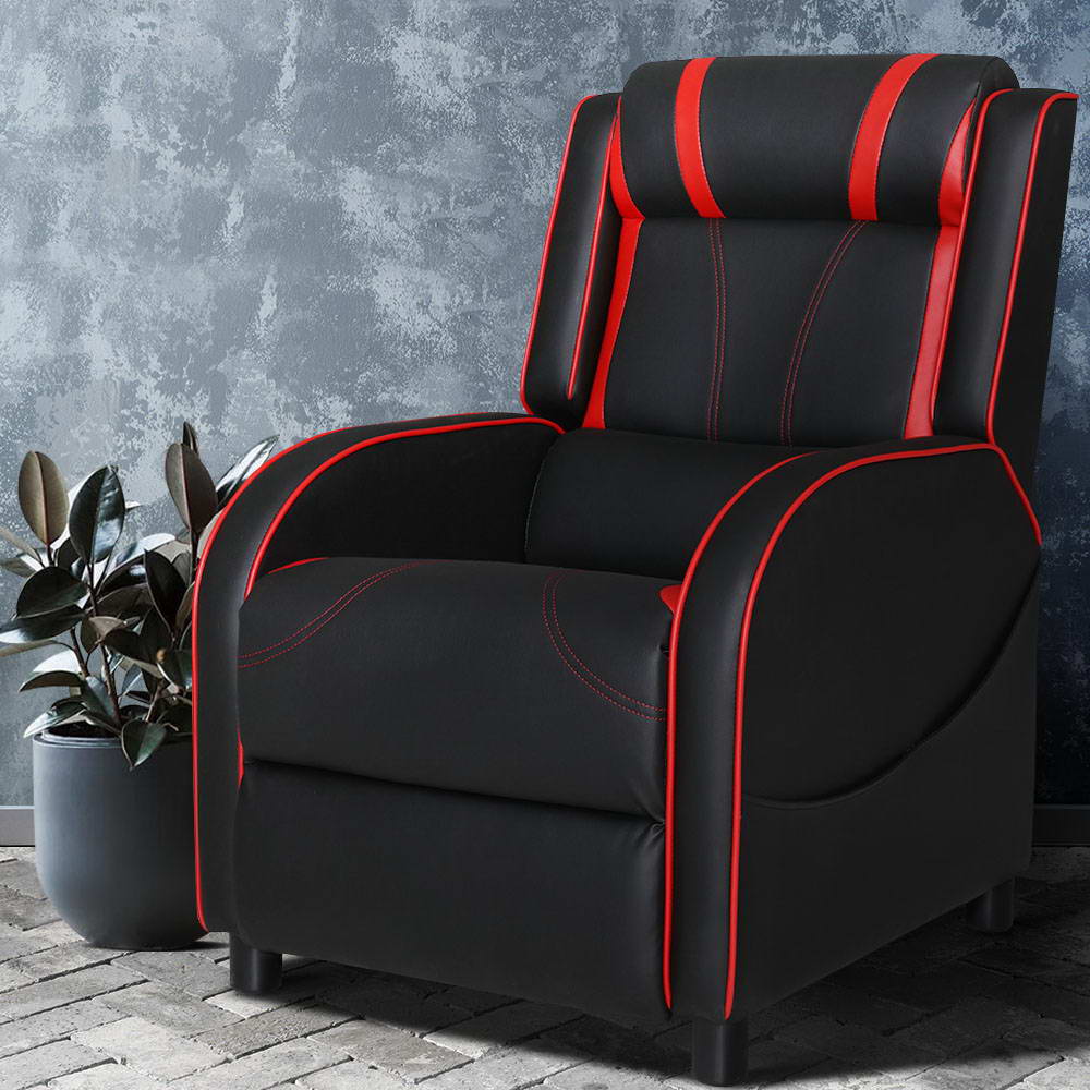 Black and red gaming recliner with red piping and neck roll headrest against concrete textured wall, lifestyle setting