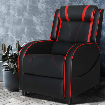 Black and red gaming recliner with red piping and neck roll headrest against concrete textured wall, lifestyle setting