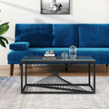 Rectangular glass-top coffee table with black metal starburst base, front-side view with blue velvet sofa and framed artwork